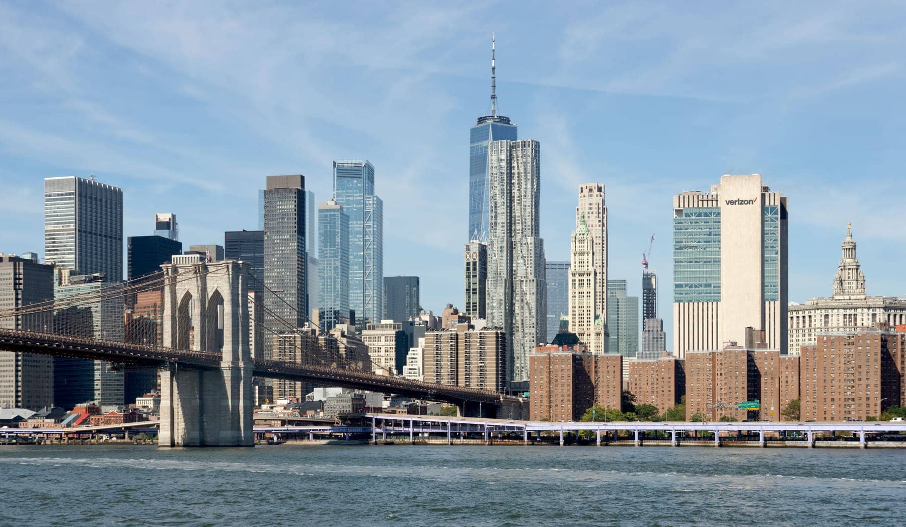 Lower Manhattan skyline and the Brooklyn Bridge seen across the East River under a blue sky